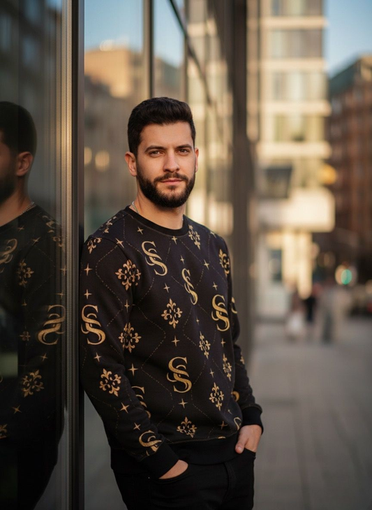 Man wearing a black sweater with gold patterns standing in an urban setting.